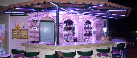 A bar with a brick facade, a counter with stools, and a variety of bottles on shelves.