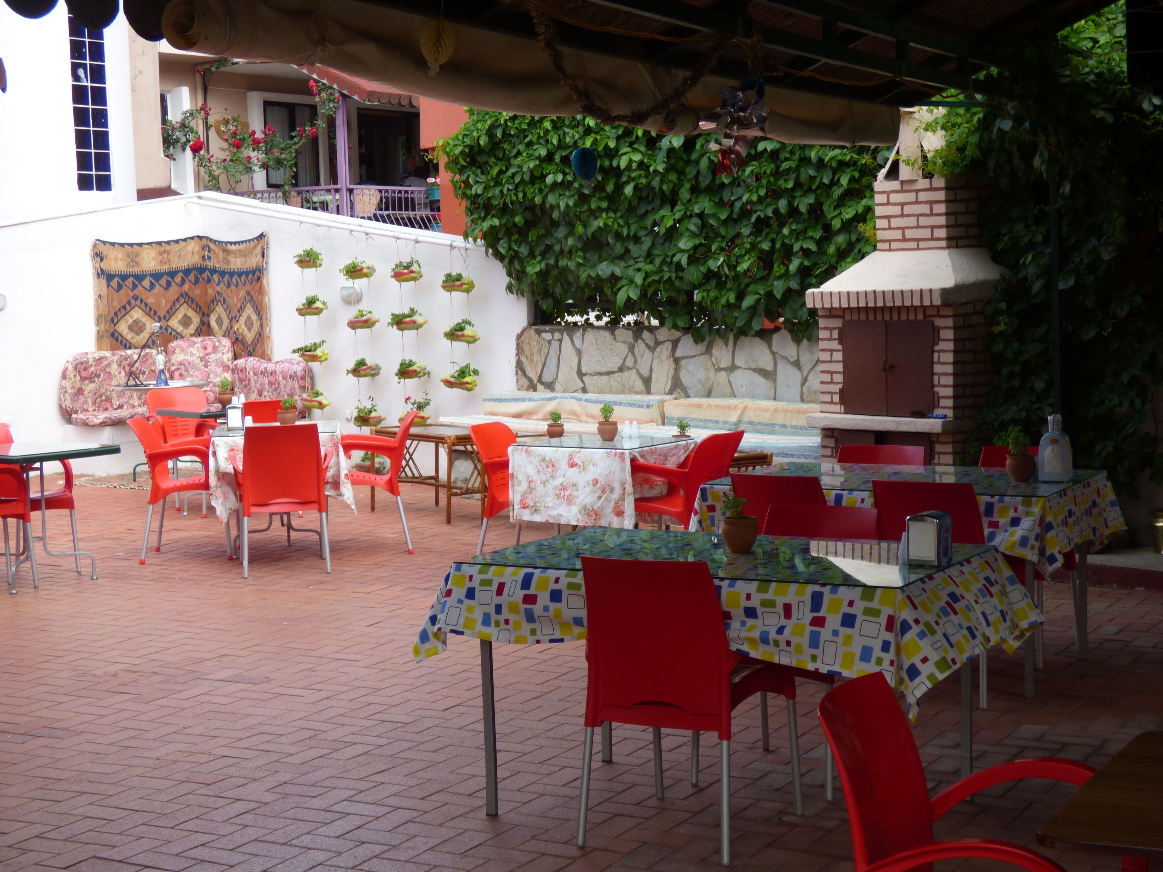 Un espacio de comedor al aire libre con sillas y mesas rojas, una pared de piedra con plantas y un arreglo colgante de plantas.