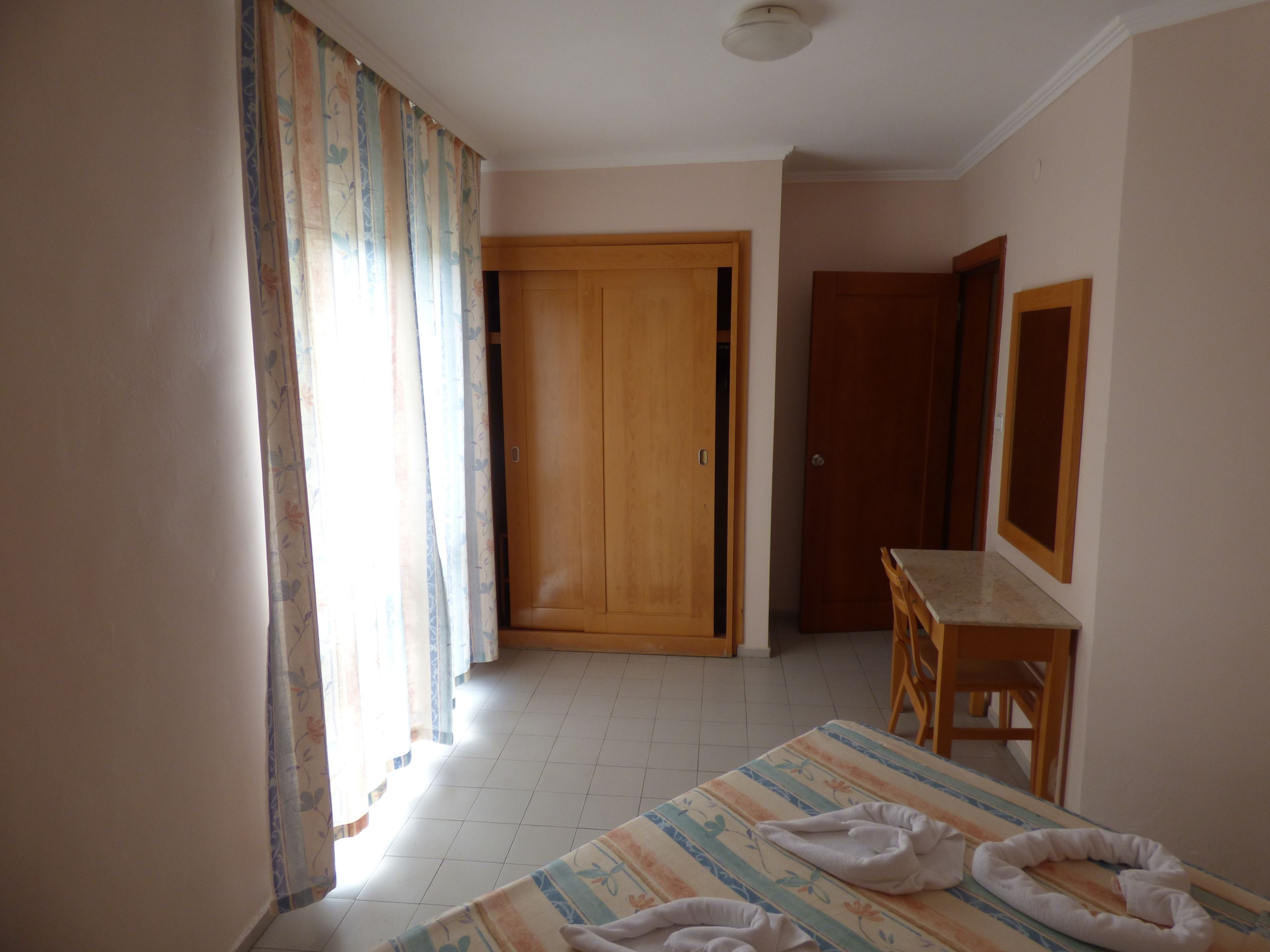 Une chambre d’hôtel avec un lit, un bureau en bois, un miroir et une armoire.