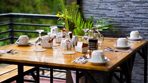 A wooden dining table set with white cups, saucers, and a variety of glassware. - Vela Terraces Hotel (Coron)