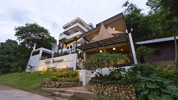 A modern hotel with a prominent name sign, multiple balconies, and a well-maintained garden area. - Vela Terraces Hotel (Coron)