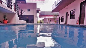 An indoor swimming pool with clear water, surrounded by a building with balconies and potted plants. - Vela Terraces Hotel (Coron)