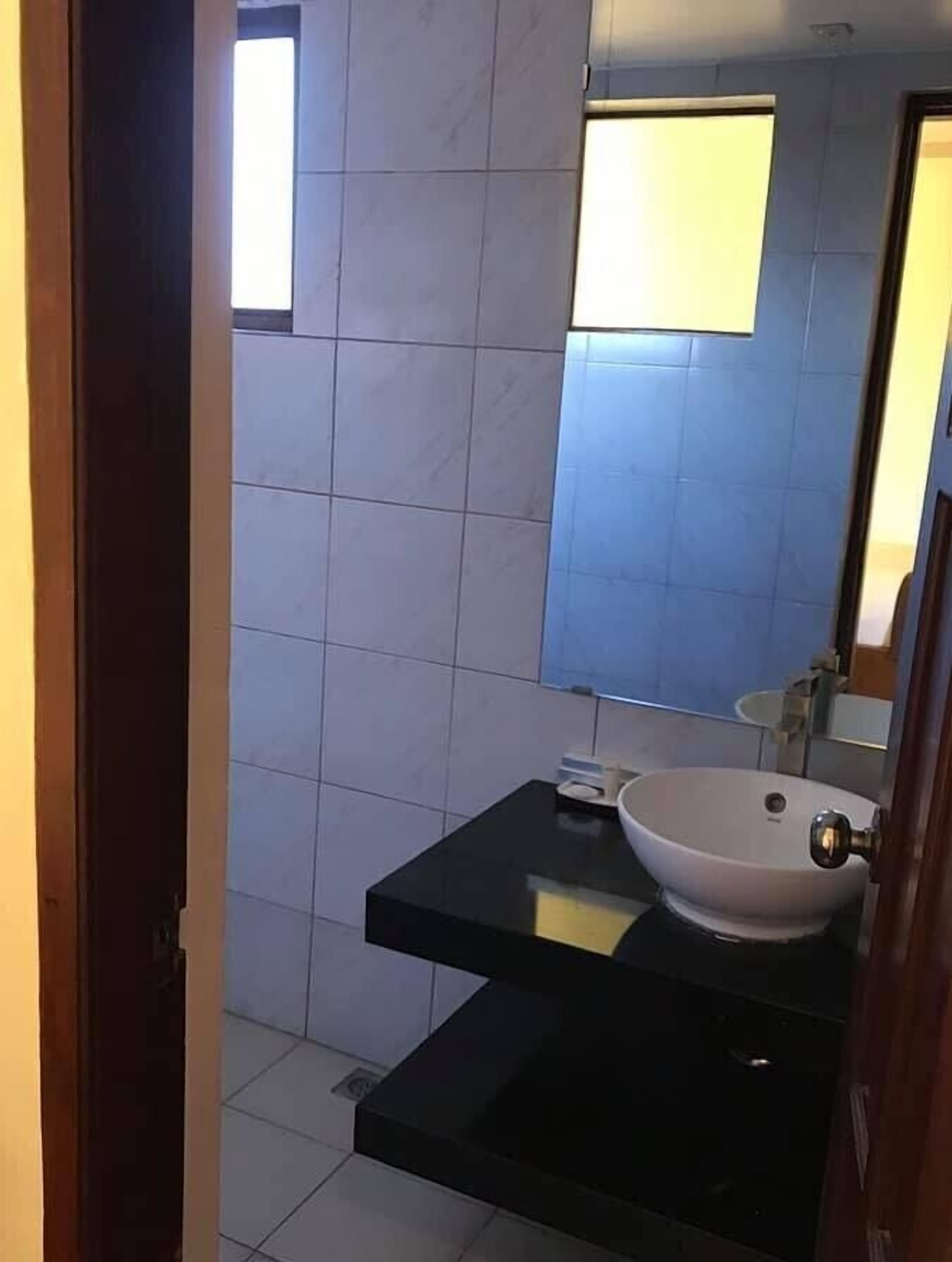 Un baño con lavamanos blanco, un espejo y un ventanal pequeño.