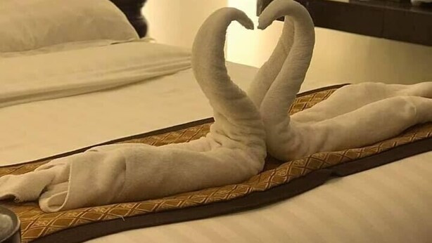 Habitación de hotel con dos camas, una de ellas con una toalla dispuesta en forma de corazón.