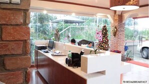 Un mostrador de recepción con una computadora, una botella de agua y una cafetera. Se ve un árbol de Navidad y una pared de ladrillo al fondo.