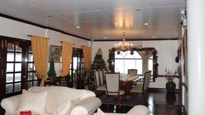 Un salón amplio con un sofá blanco, una zona de comedor con un árbol de Navidad y una araña.