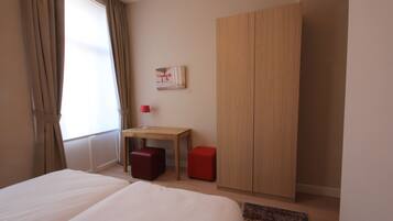 Un dormitorio con cama, escritorio, armario y ventana con cortinas.