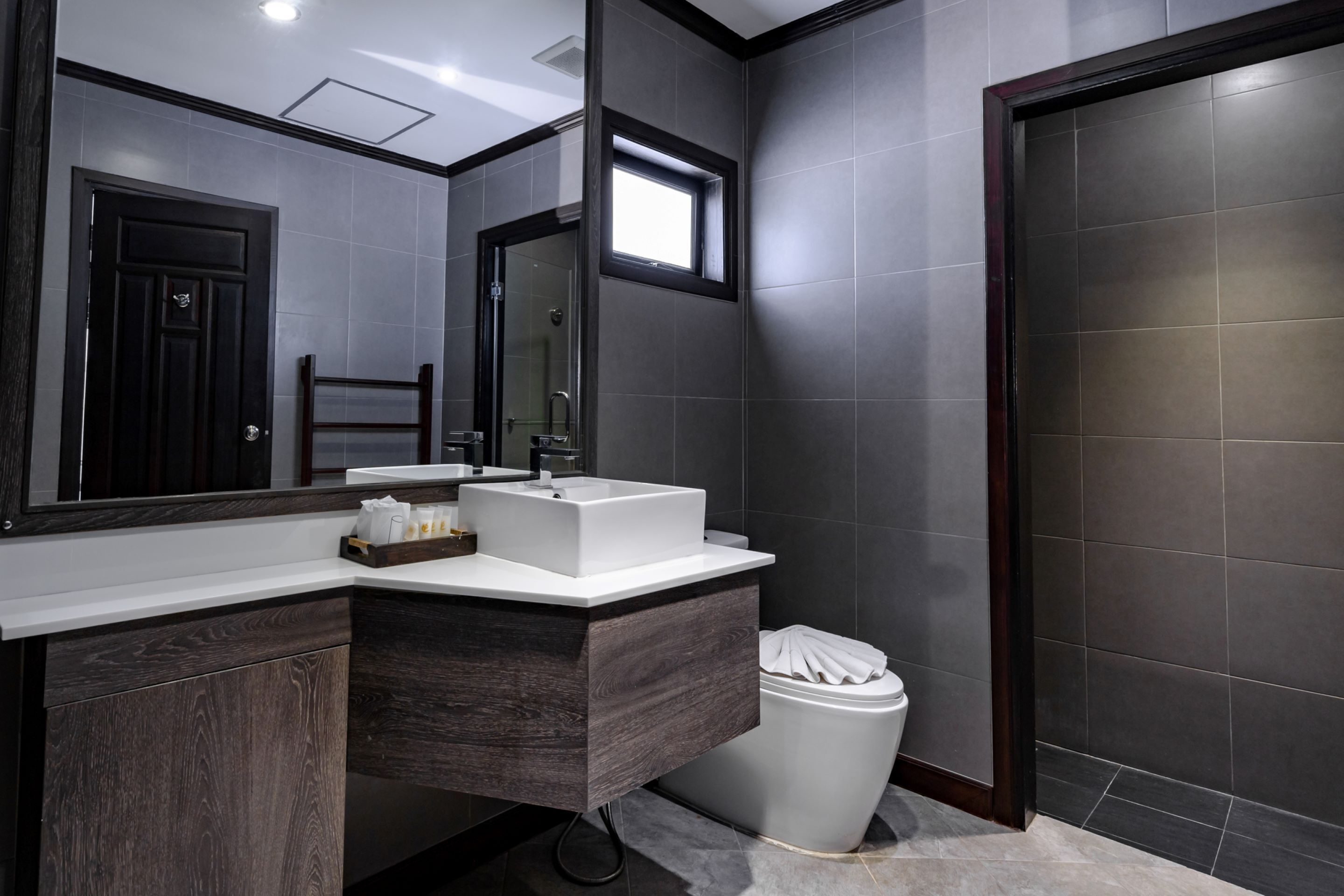 A modern bathroom with a dark wood vanity, a white sink, and a large mirror.