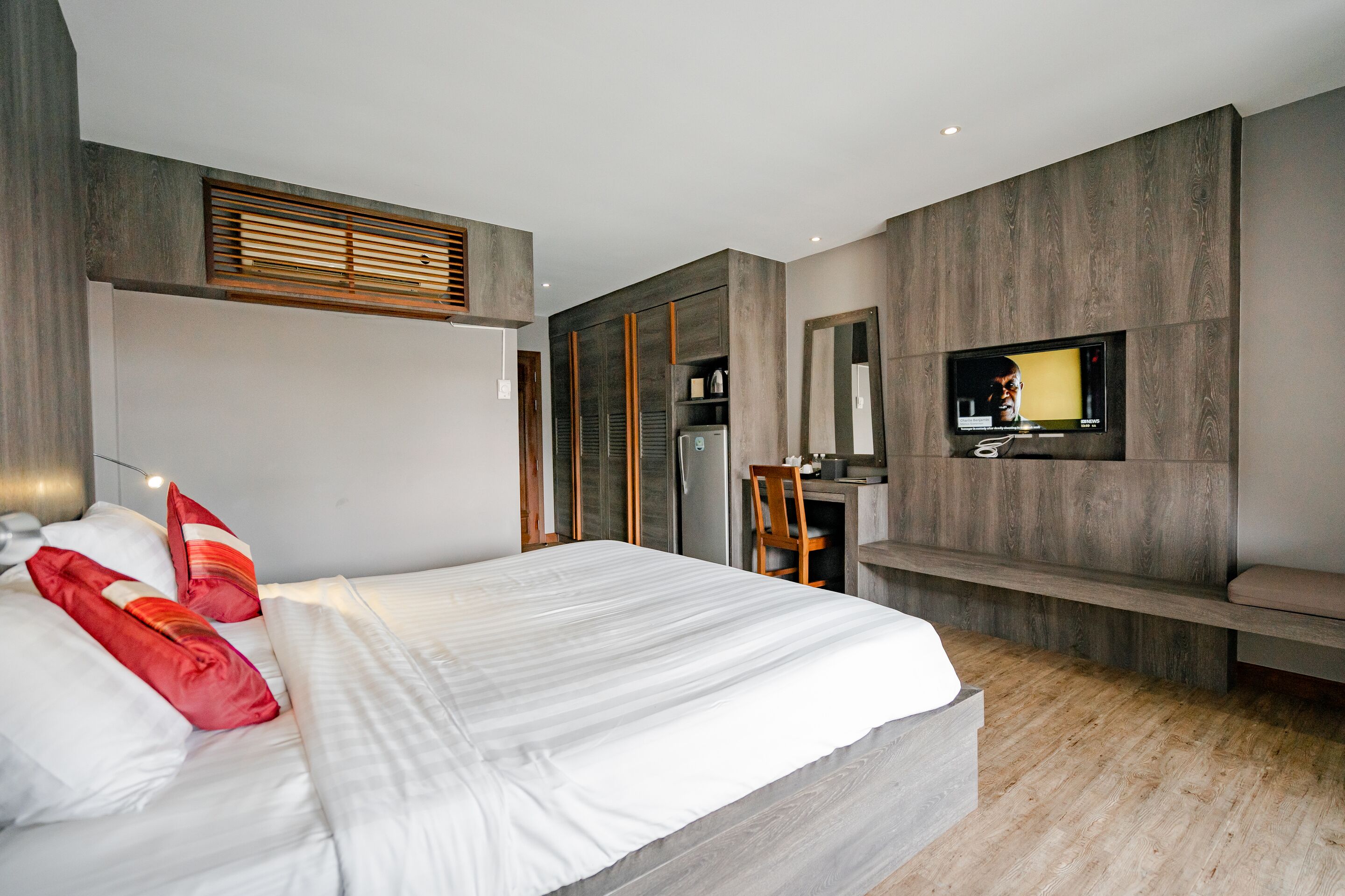 A modern bedroom with a large bed, a TV mounted on the wall, and a small desk area.