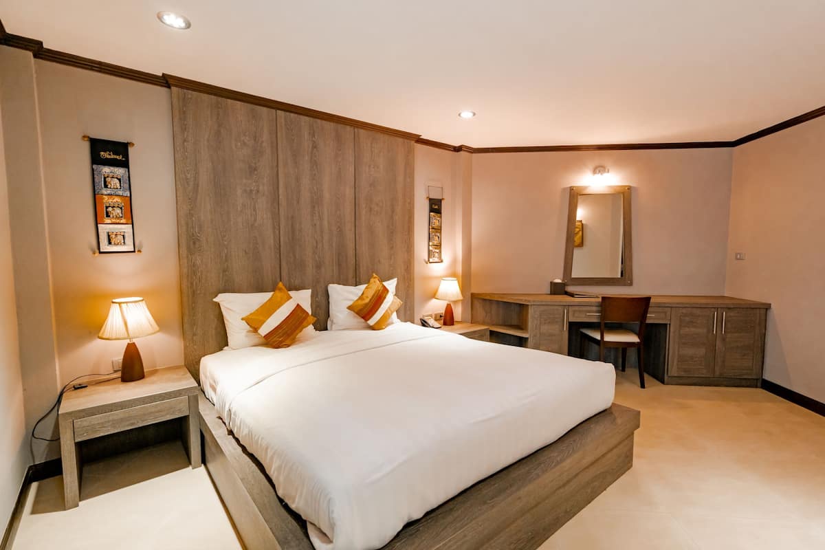 A hotel room with a large bed, bedside tables with lamps, a desk, and a mirror.