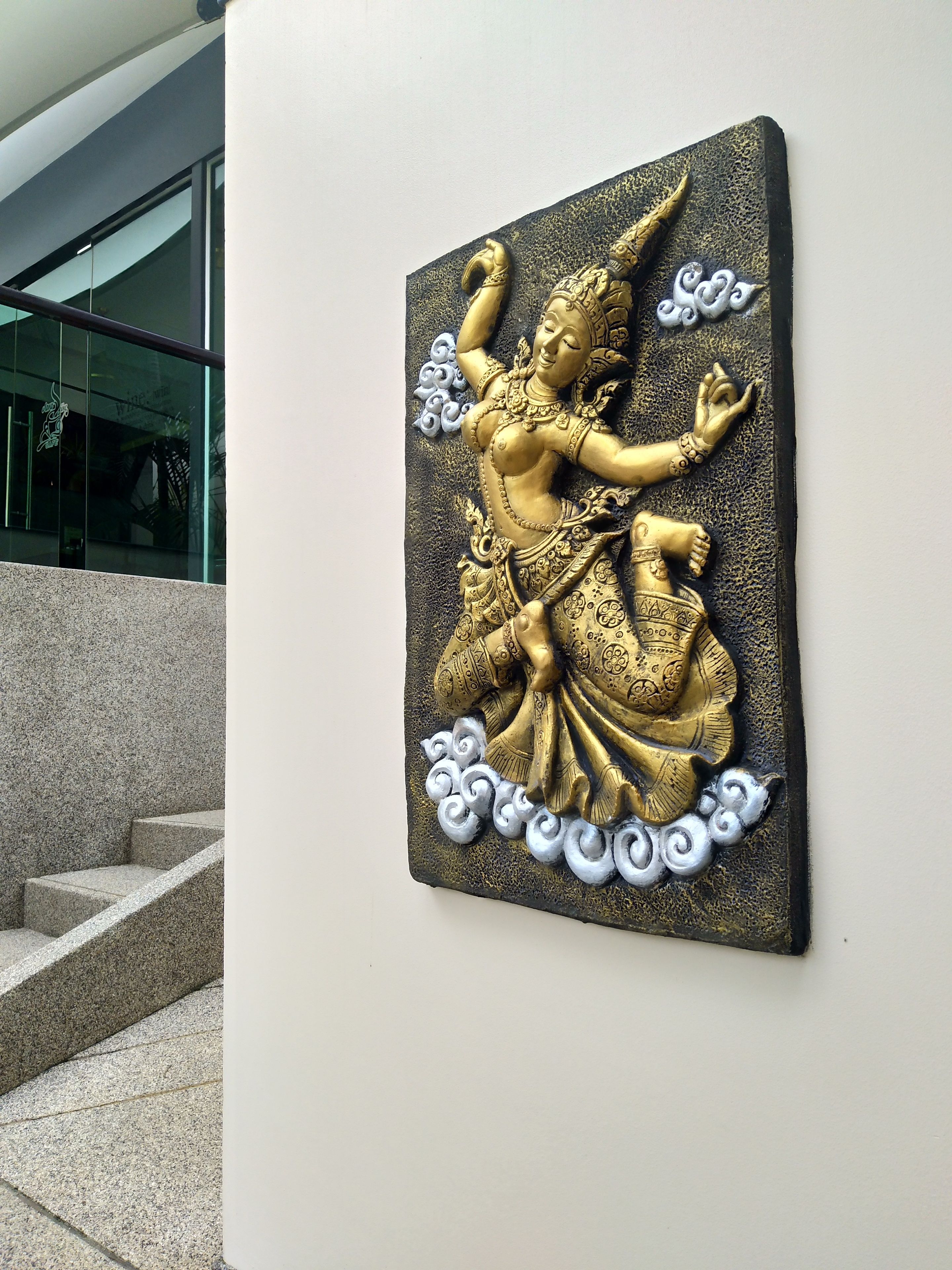 Una escultura en la pared que representa a una deidad sentada, con vestimentas y joyas elaboradas.