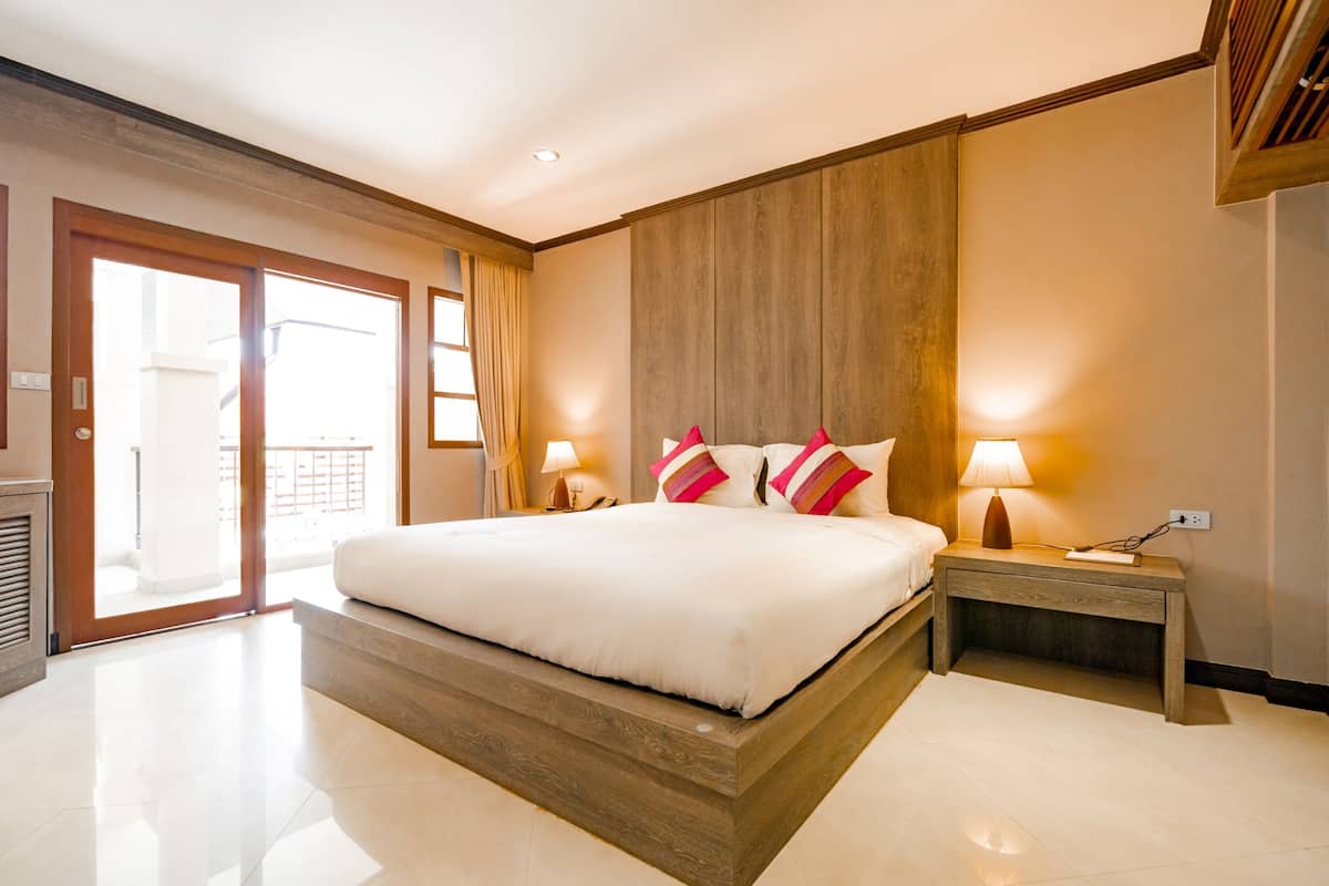 A spacious bedroom with a large bed, wooden headboard, and a nightstand with a lamp.