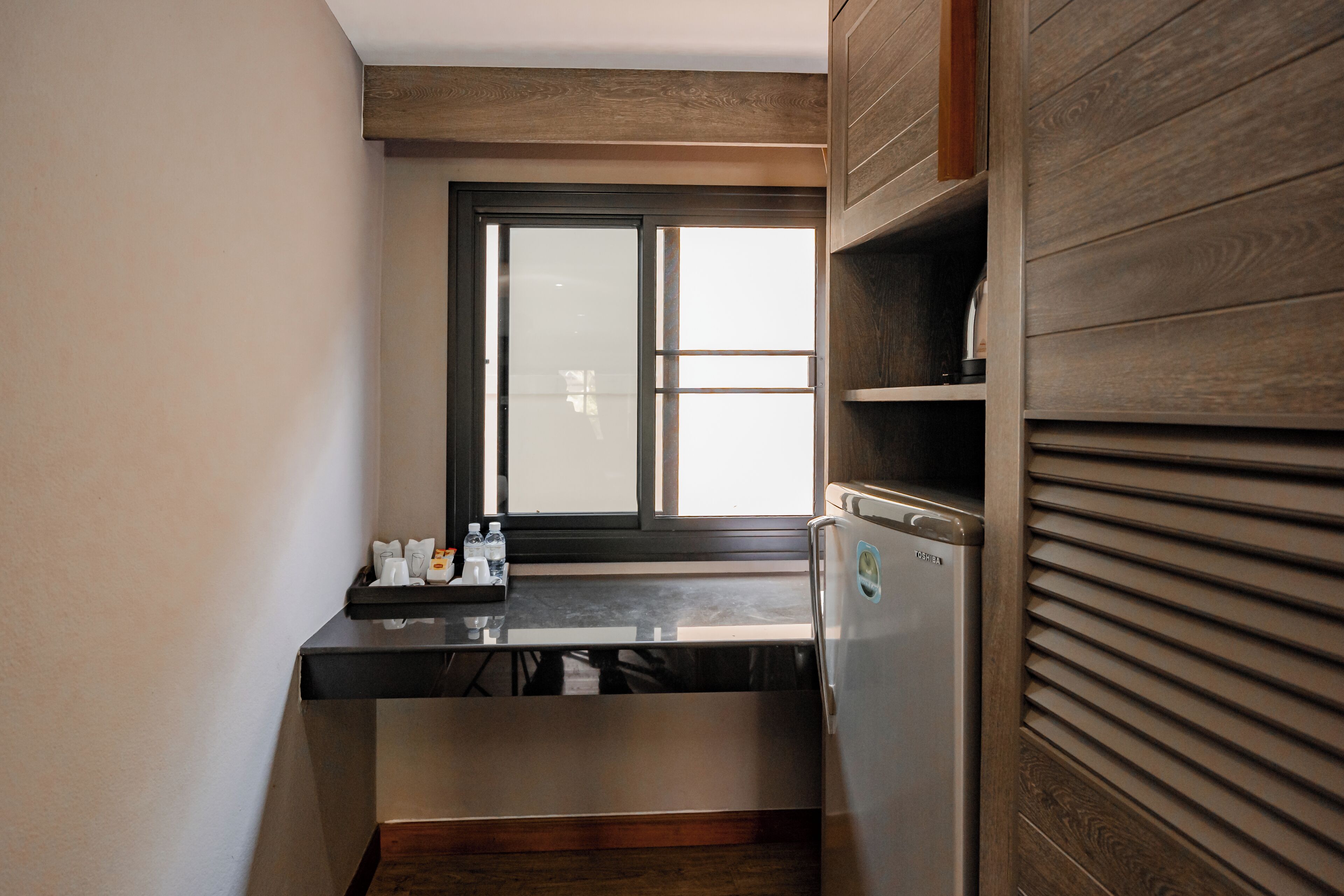 A compact kitchen with a built-in refrigerator, a window with blinds, and a countertop with a few items.