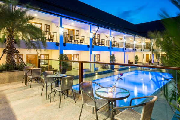 A hotel with a pool, outdoor seating, and a two-story structure.