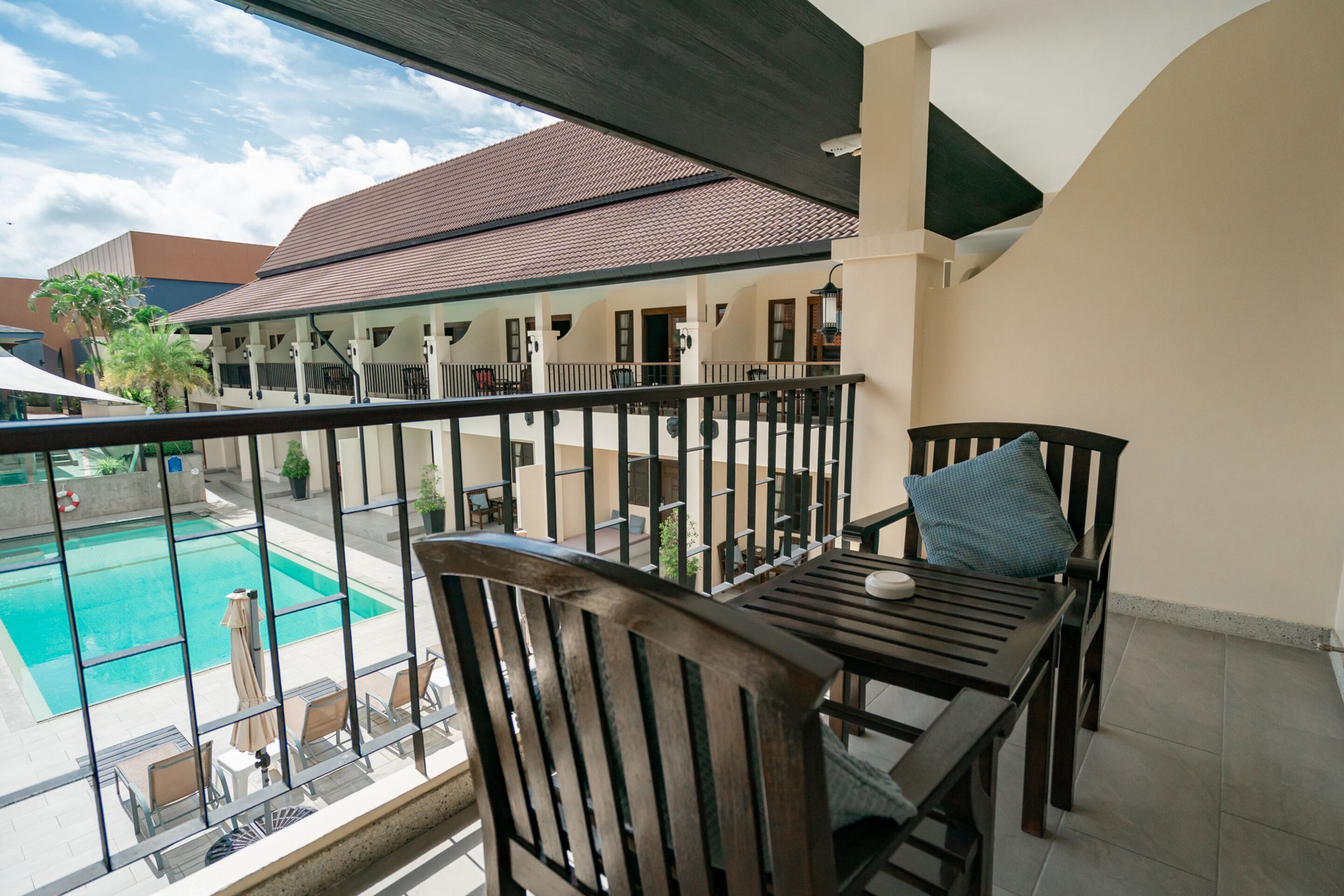 A balcony with a view of a swimming pool, a table with chairs, and a railing.