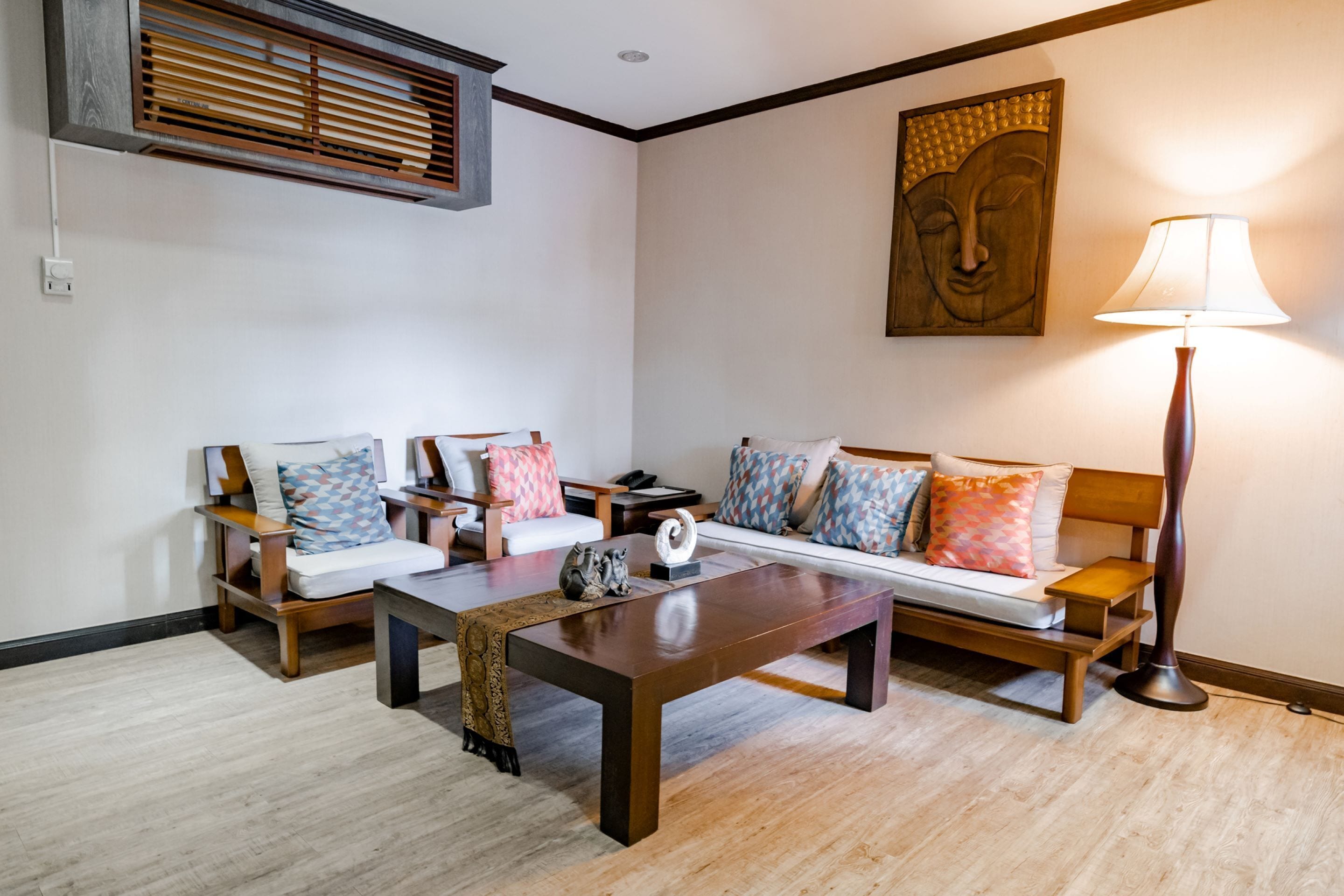 A living room with a sofa, two armchairs, a coffee table, a floor lamp, and a wall-mounted air conditioning unit.