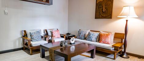 A living room with a sofa, two armchairs, a coffee table, a floor lamp, and a wall-mounted air conditioning unit.