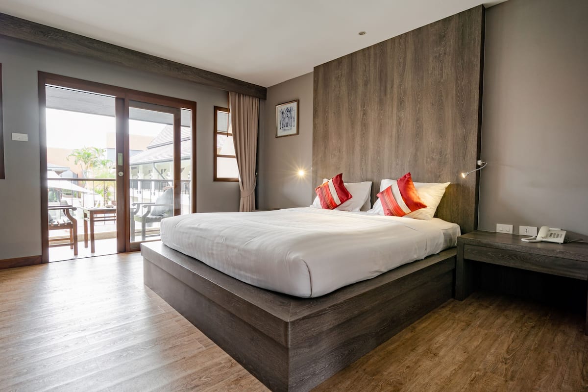 A modern hotel room with a large bed, a wooden headboard, a desk with a phone, and a view of the outdoor area through a sliding door.