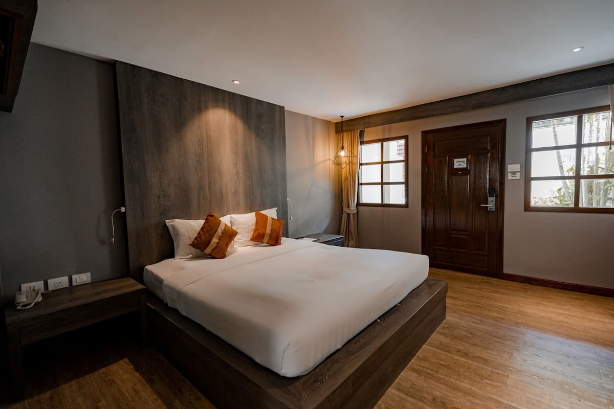 A modern hotel room with a large bed, wooden headboard, and a view of palm trees through the window.