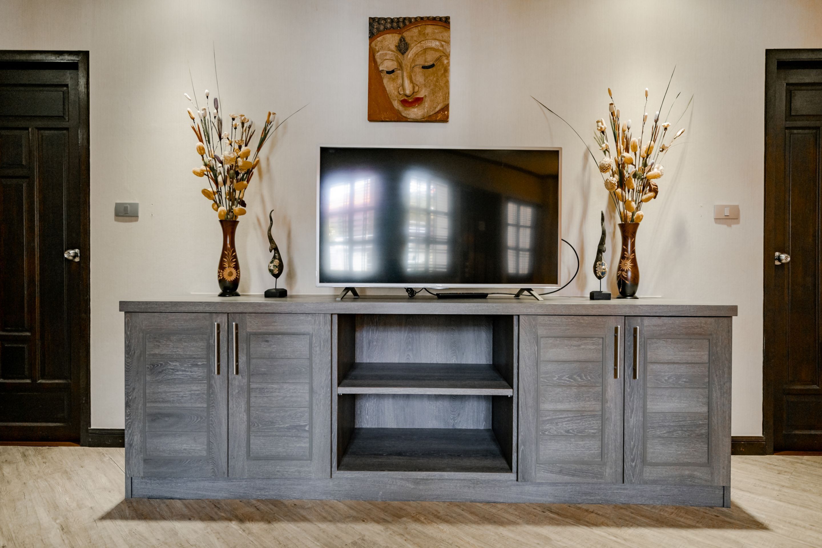 Una sala de estar moderna con un mueble gris para el equipo de entretenimiento, un televisor de pantalla plana y dos jarrones decorativos.