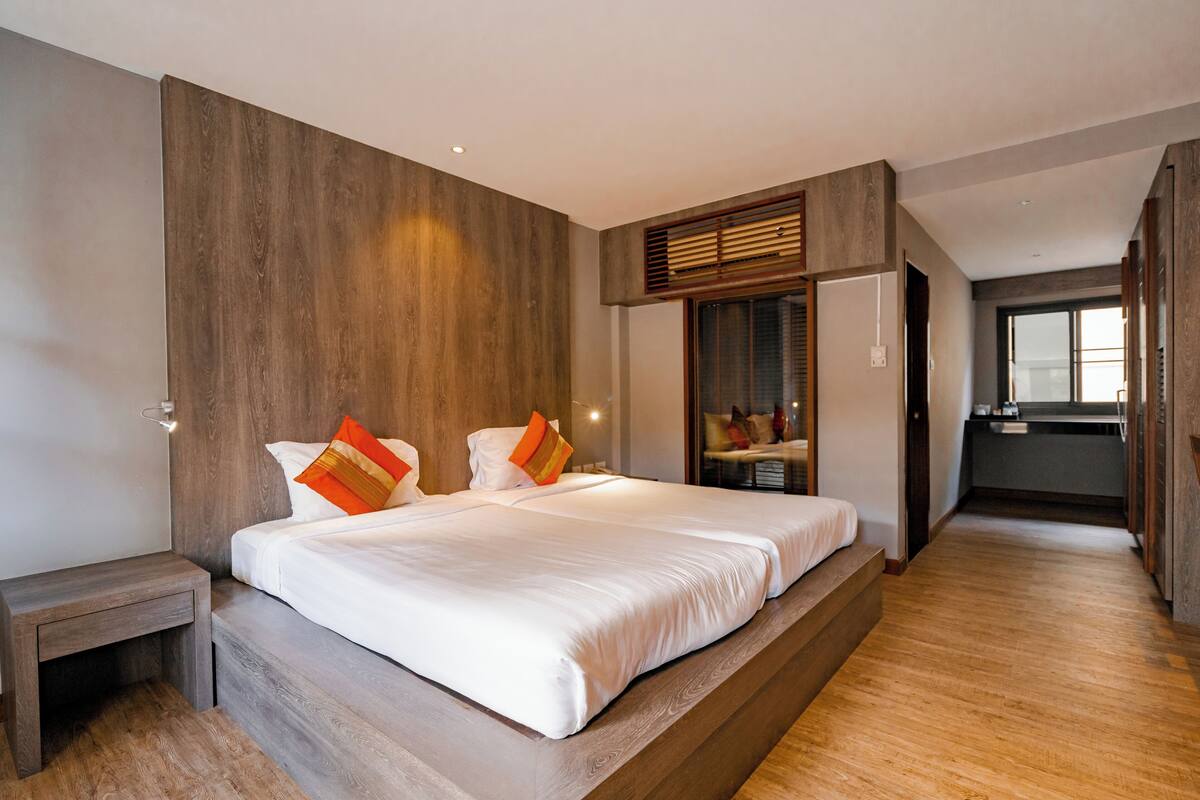 A modern bedroom with a large bed, wooden paneling on the walls, and a view into the kitchen area.