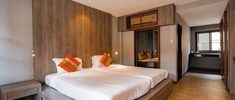 A modern bedroom with a large bed, wooden paneling on the walls, and a view into the kitchen area.