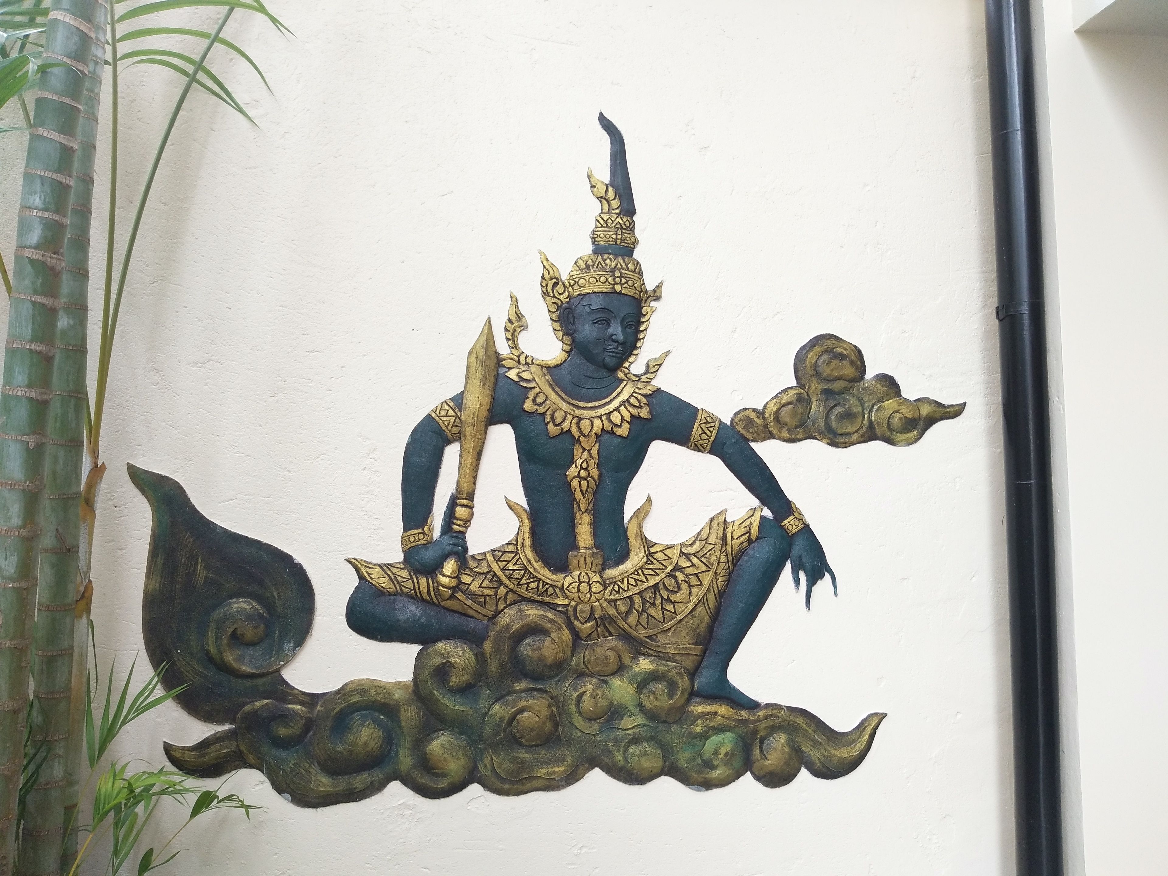 Decorativa obra de arte de una figura mítica con tocado dorado y atuendo negro y dorado, sentada sobre una base que parece una nube.