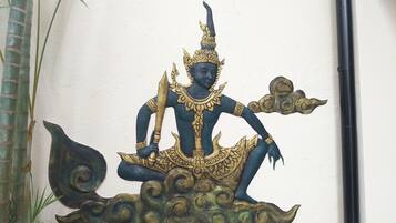 Decorativa obra de arte de una figura mítica con tocado dorado y atuendo negro y dorado, sentada sobre una base que parece una nube.