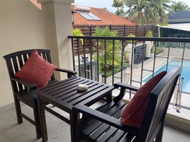 Un balcón con mesa y sillas, una piscina y vistas a un edificio con techo de tejas rojas.