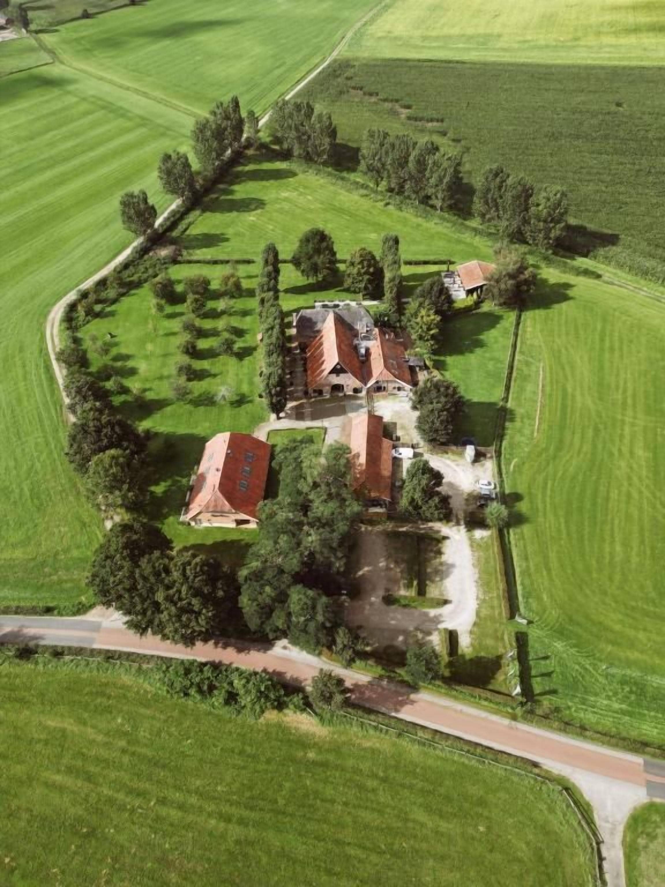 Vista aérea de una propiedad con varias edificaciones, rodeada de campos verdes y árboles.