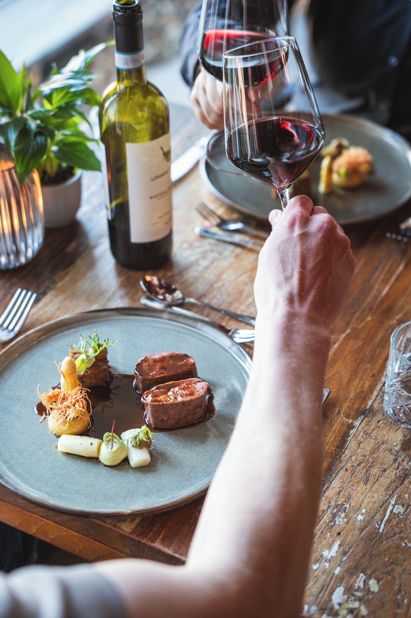 A dining table with plates of food, a bottle of wine, and a glass of wine.