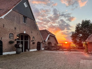 Un bâtiment en briques avec une cour pavée, une clôture en bois et un coucher de soleil en arrière-plan.