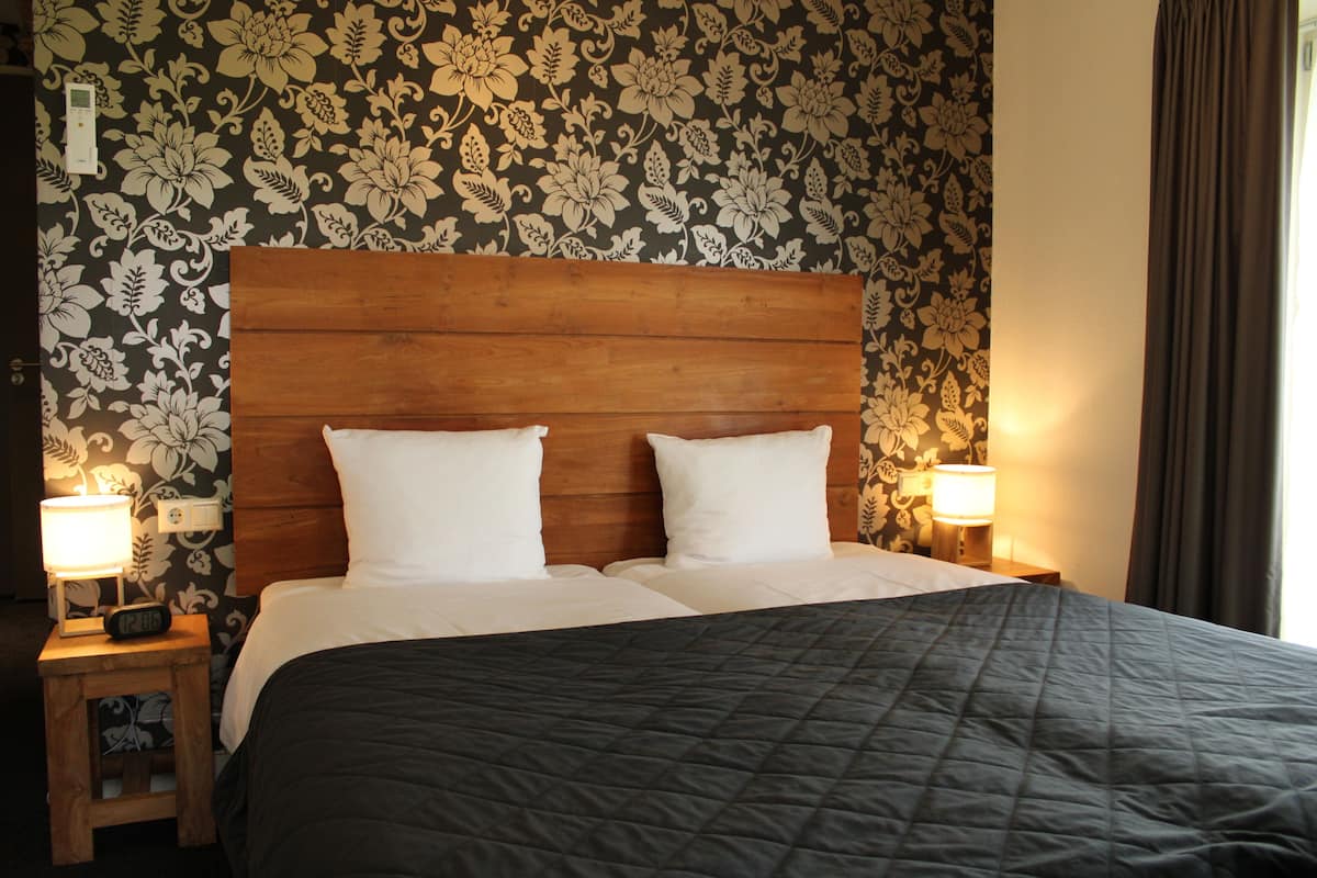 A hotel room with a large bed, two bedside lamps, a wooden headboard, and floral wallpaper.