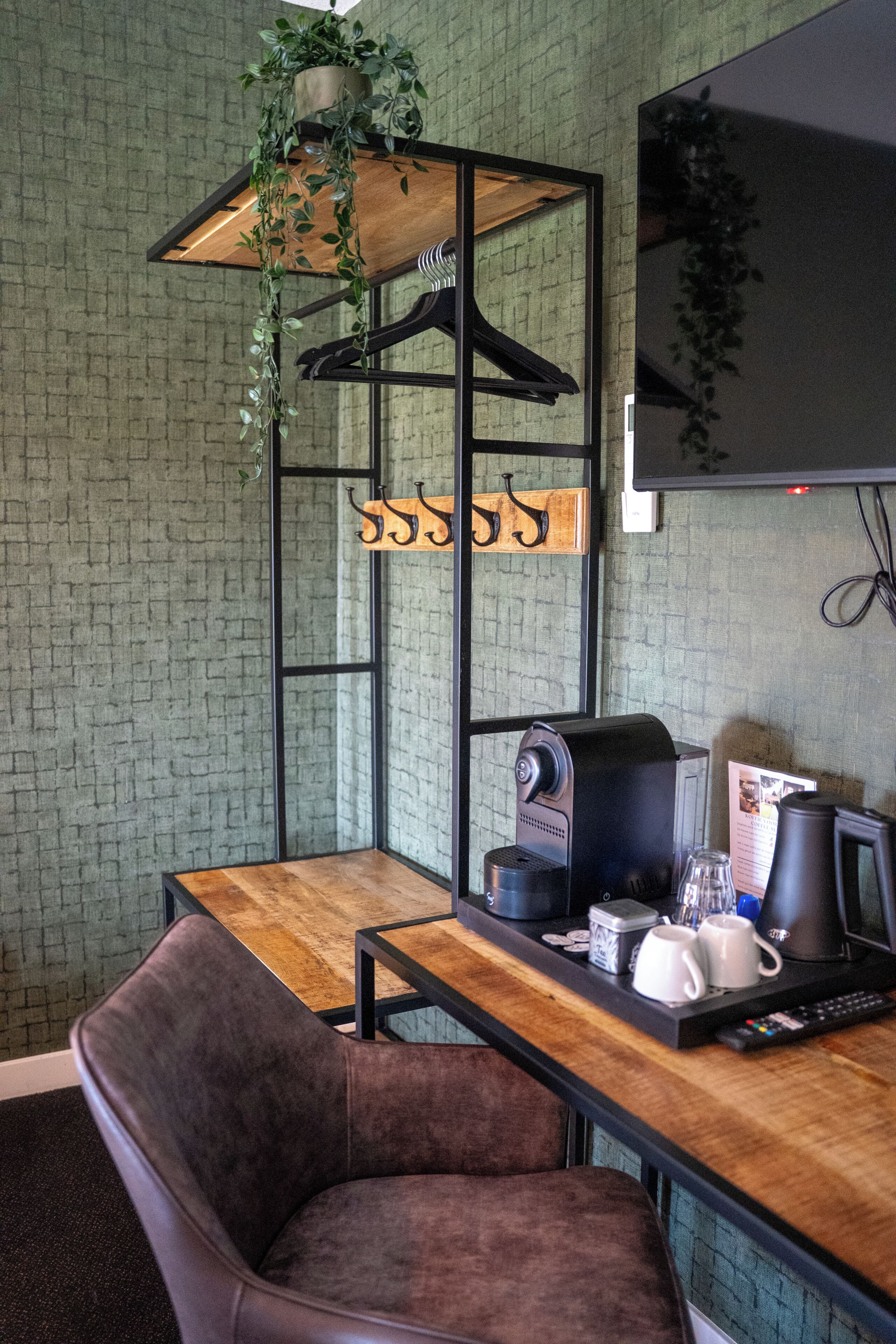 Una habitación con pared de ladrillo, una mesa de madera, una silla marrón, una máquina de café y un televisor montado en la pared.