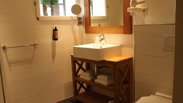 Un bagno con lavandino bianco, mensole in legno, porta asciugamani, uno specchio e una finestra con piante.