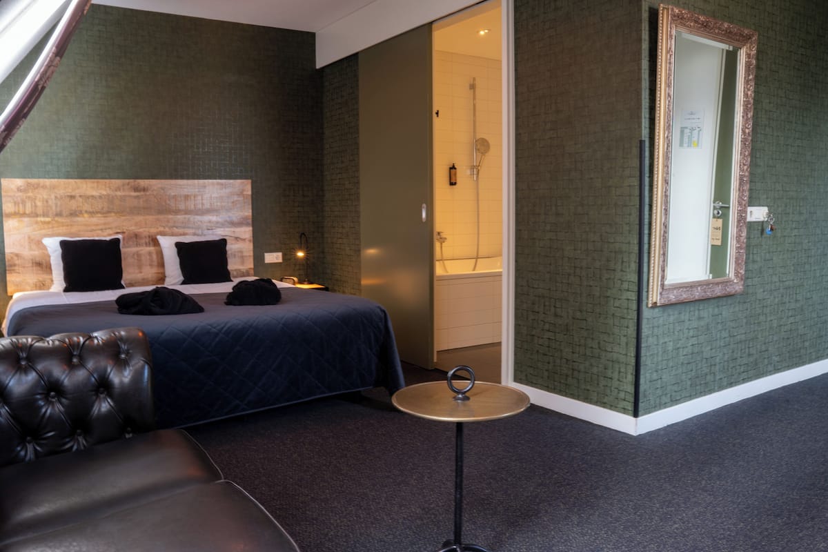A hotel room with a bed, a round table, a mirror, and a shower area.