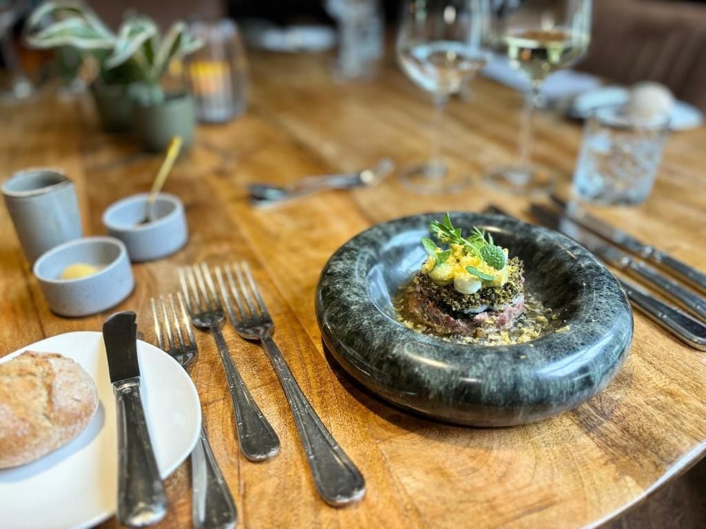 Una mesa con un plato de comida, cubiertos y una copa de vino.