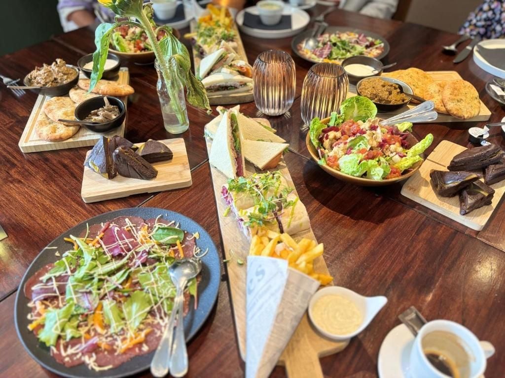 Una mesa de comedor con diversos platos, entre ellos ensaladas, sándwiches y pan.