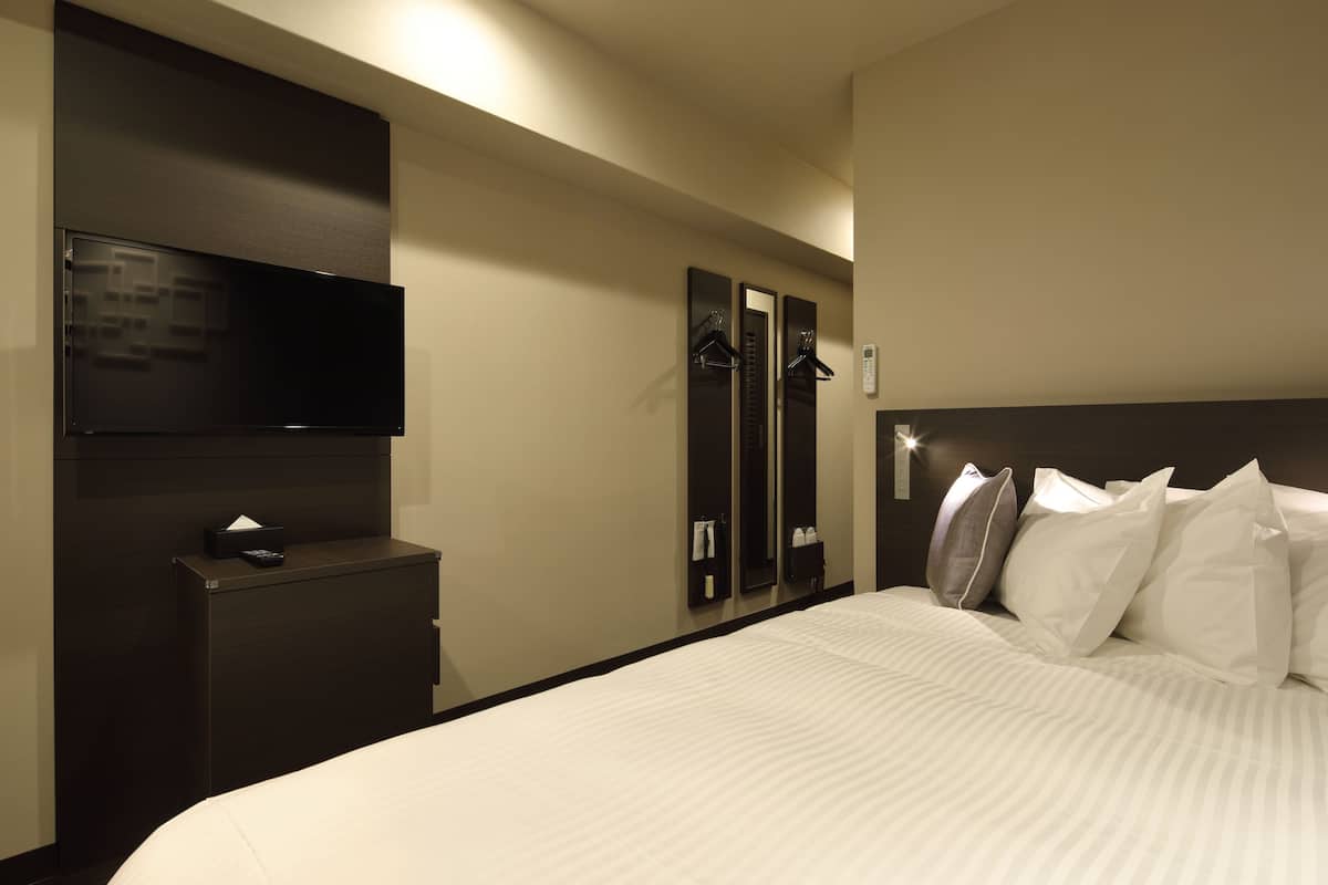 Une chambre d’hôtel avec un grand lit, un téléviseur à écran plat fixé au mur, une commode et un miroir.