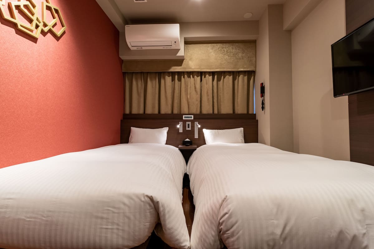 Une chambre d’hôtel avec deux lits, une télévision, un climatiseur et une fenêtre avec des rideaux.