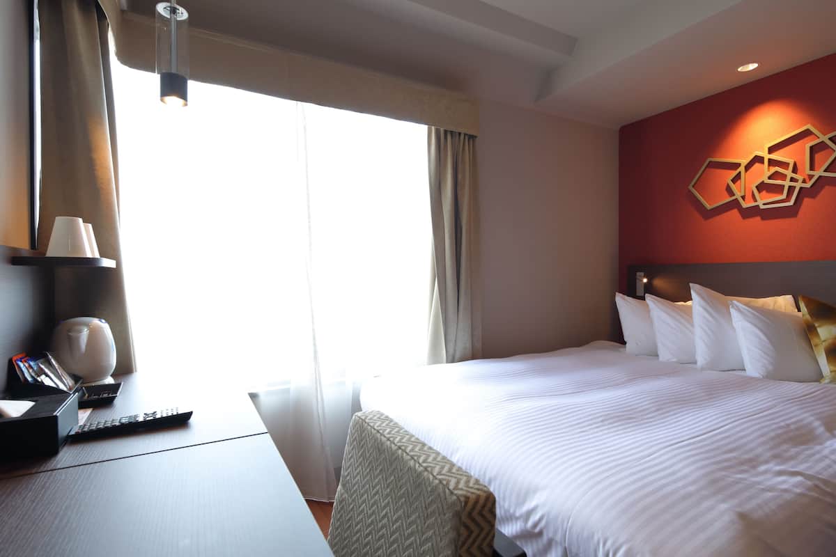 Une chambre d’hôtel avec un lit, un bureau avec un ordinateur, une lampe et une fenêtre avec des rideaux.