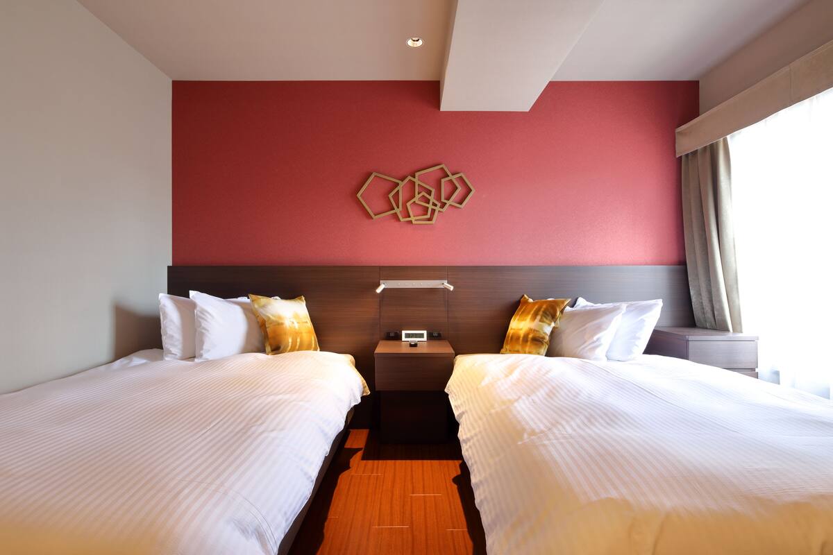 Une chambre d’hôtel avec deux lits, un mur d’accent rouge et un élément de décoration moderne au-dessus des lits.