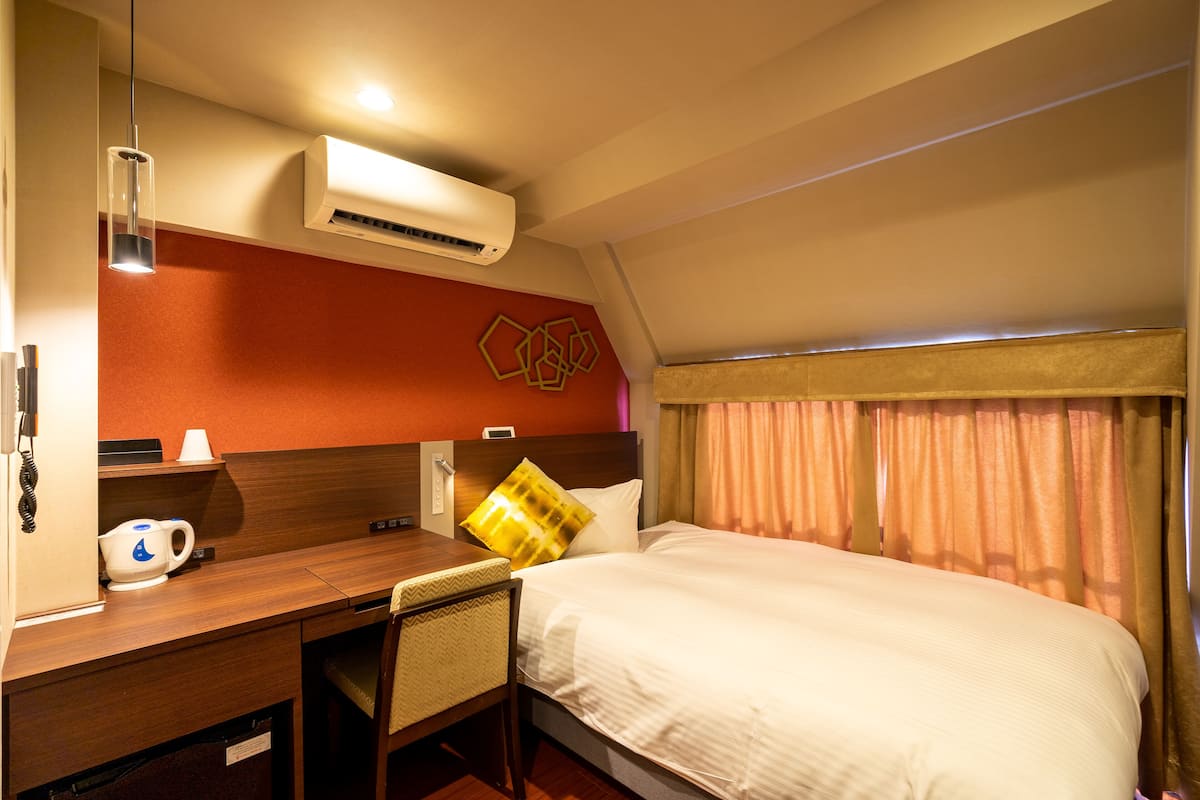 Une chambre d’hôtel équipée d’un lit, d’un bureau, d’une chaise, d’un climatiseur et d’une fenêtre avec des rideaux.