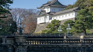 A traditional Japanese castle with a stone wall, wooden buildings, and a bridge.