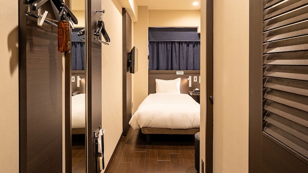 A narrow hallway leading to a bedroom with a bed, a mirror, and a coat rack.