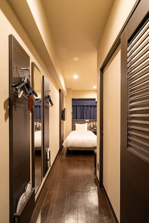 A narrow hallway leading to a bedroom with a bed, a mirror, and a coat rack. - Red Roof Inn Kamata (Tokyo)