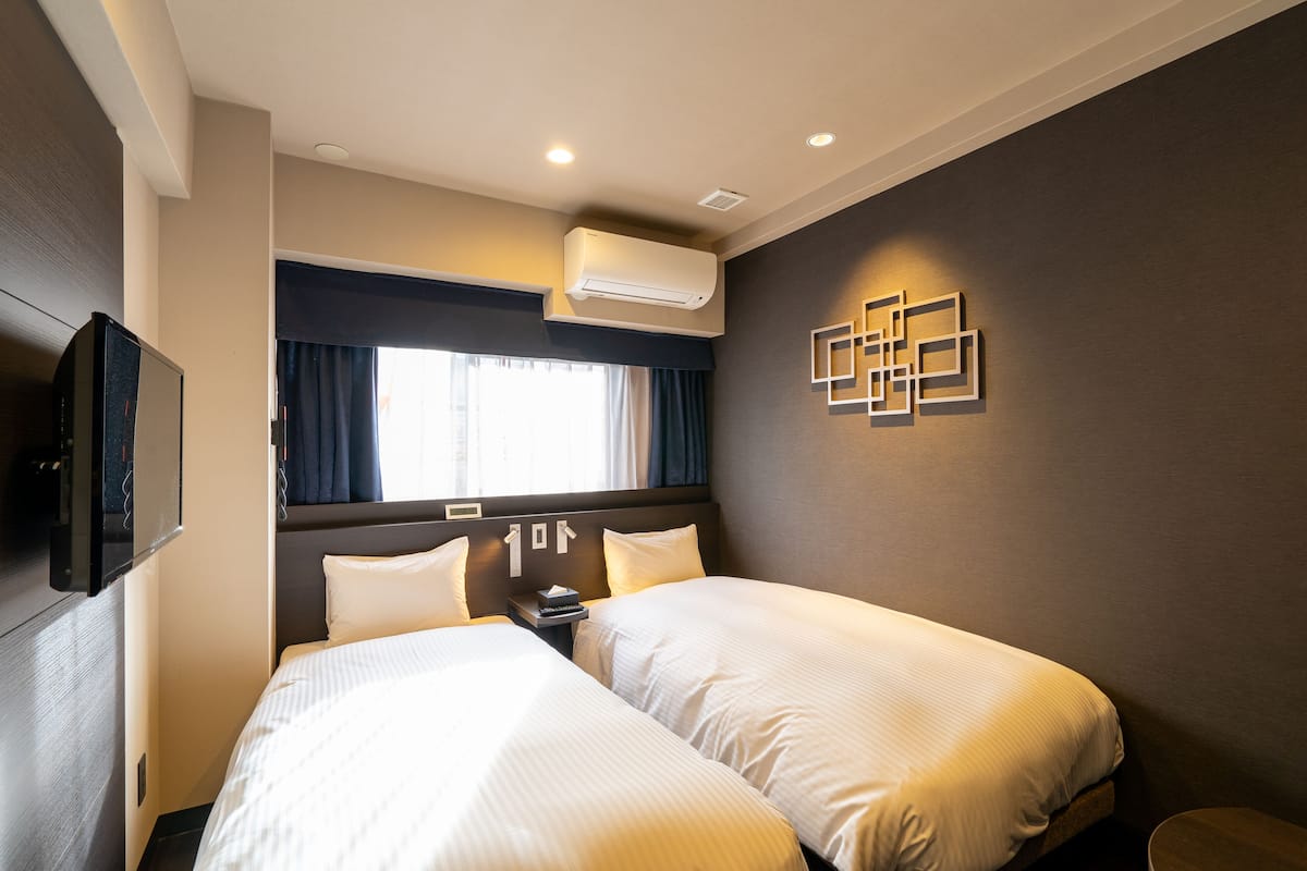 Une chambre d’hôtel avec deux lits, un téléviseur à écran plat, un appareil de climatisation et une fenêtre avec des rideaux.