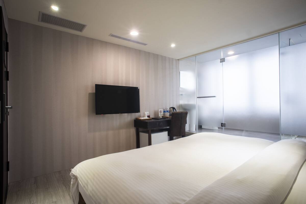 Une chambre d’hôtel moderne dotée d’un grand lit, d’un bureau avec une chaise, d  ’un téléviseur à écran plat fixé au mur et d’un dressing.