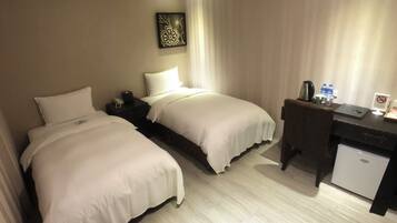 A hotel room with two beds, a desk, a chair, a small fridge, and a decorative wall piece.