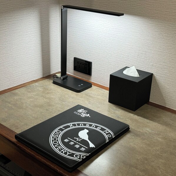 A desk with a black lamp, a tissue box, and a black notebook with white text. - Xin She Hotel - Chungli (Taoyuan City)